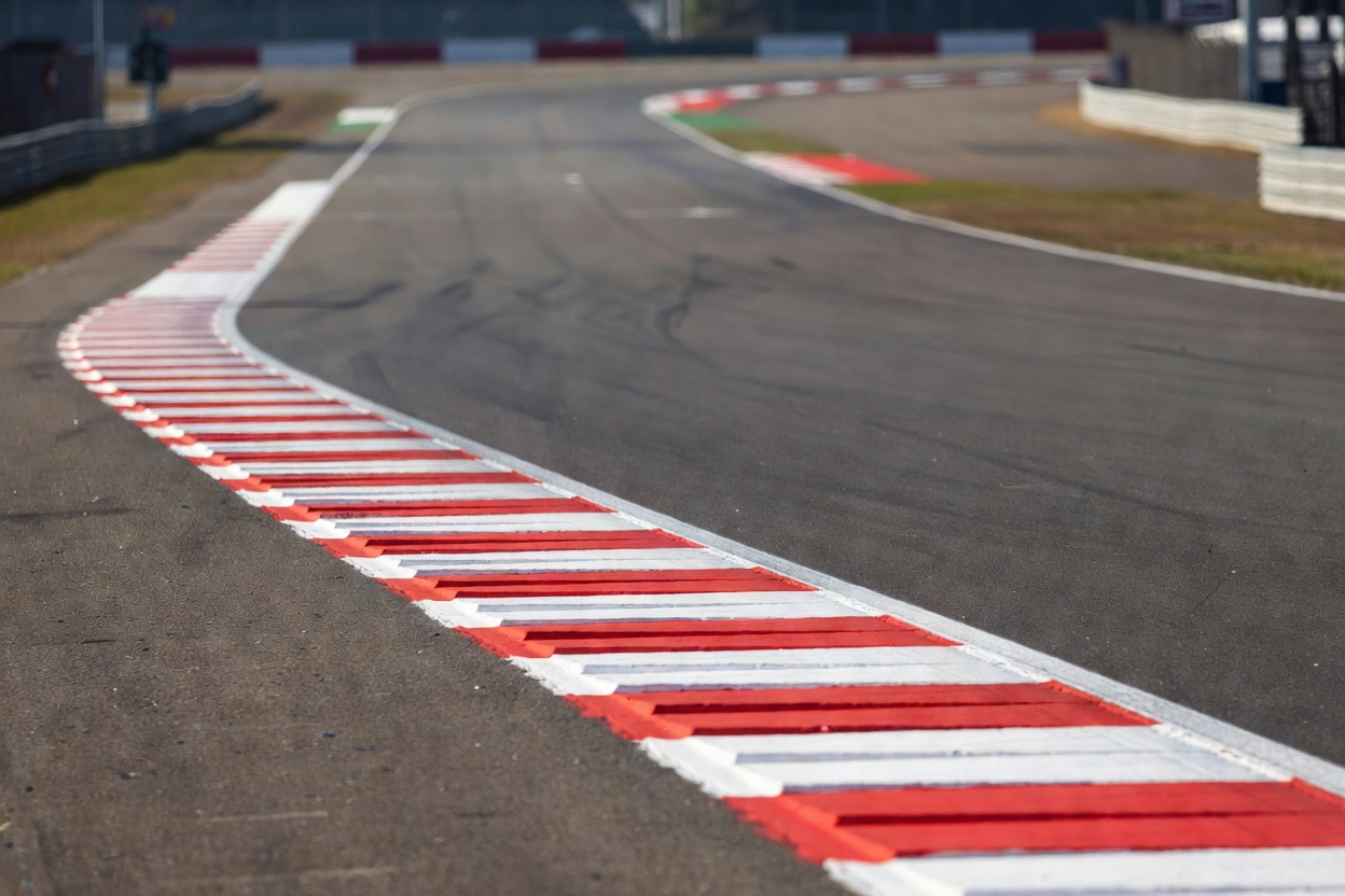Low view across a racing circuit apex, with the kerb and distant track softly blurred